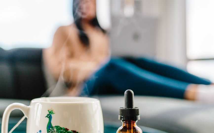 bottle of cbd drops next to cup with hot drink