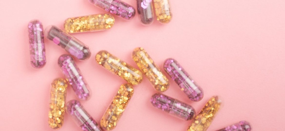 pile of sparkling drug capsules scattered on pink surface